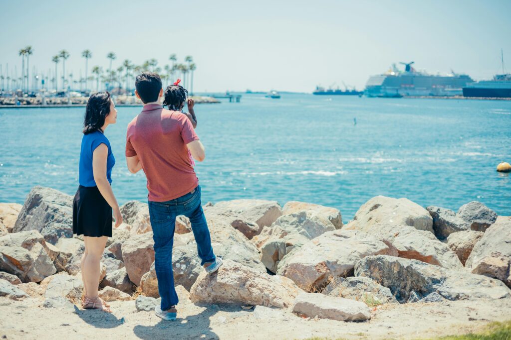 A multicultural family enjoys a sunny day by the sea with cruise ships in the background.